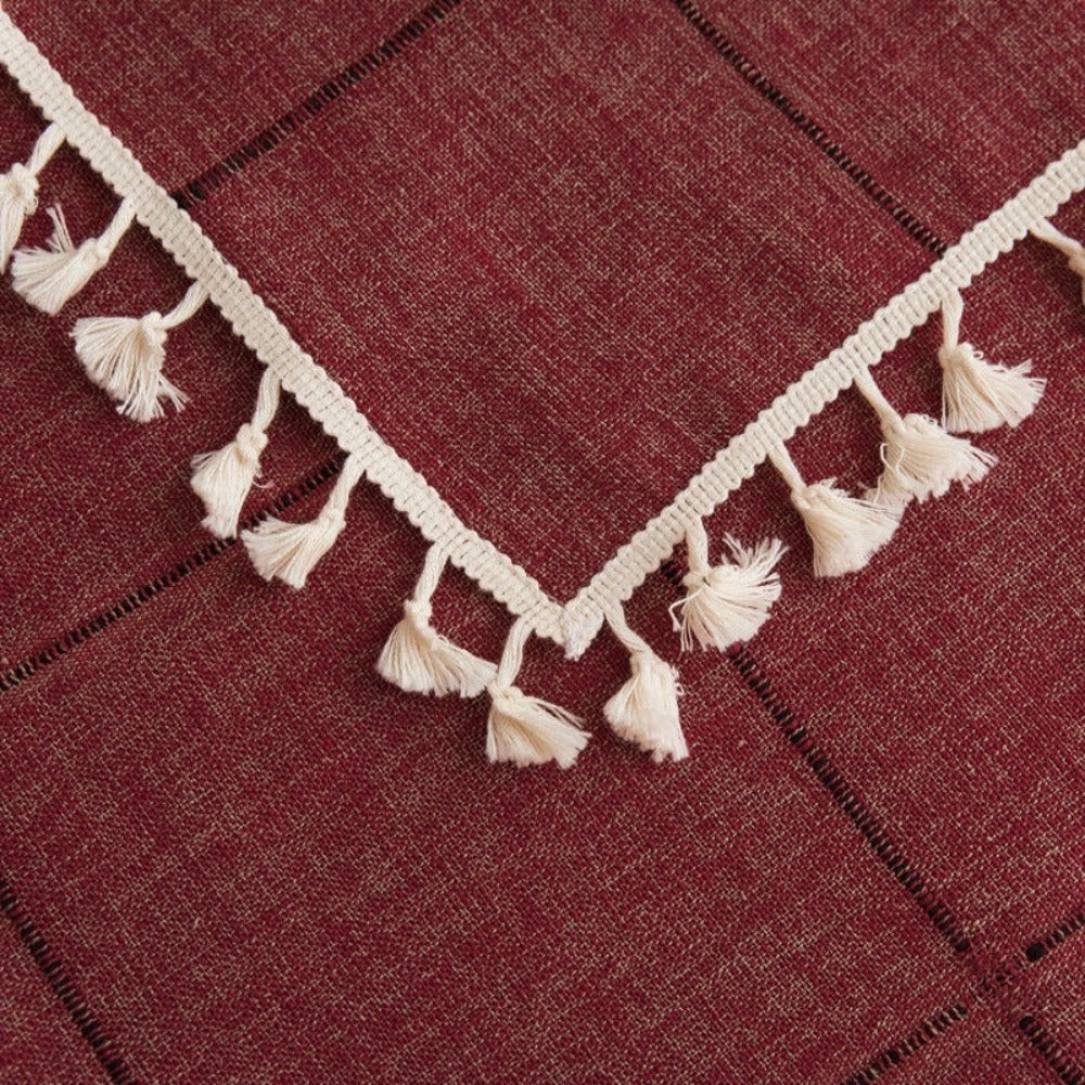 Mantel rectangular burdeo bordado y con borlas beige en su borde, ideal para decorar tu mesa de comedor, comedor de diario y mesas en general. Mantel Rectangular Color: Burdeo Diseño: Cuadros bordados con detalle en vértices color negro y borlas en todo el borde. Material: Lino